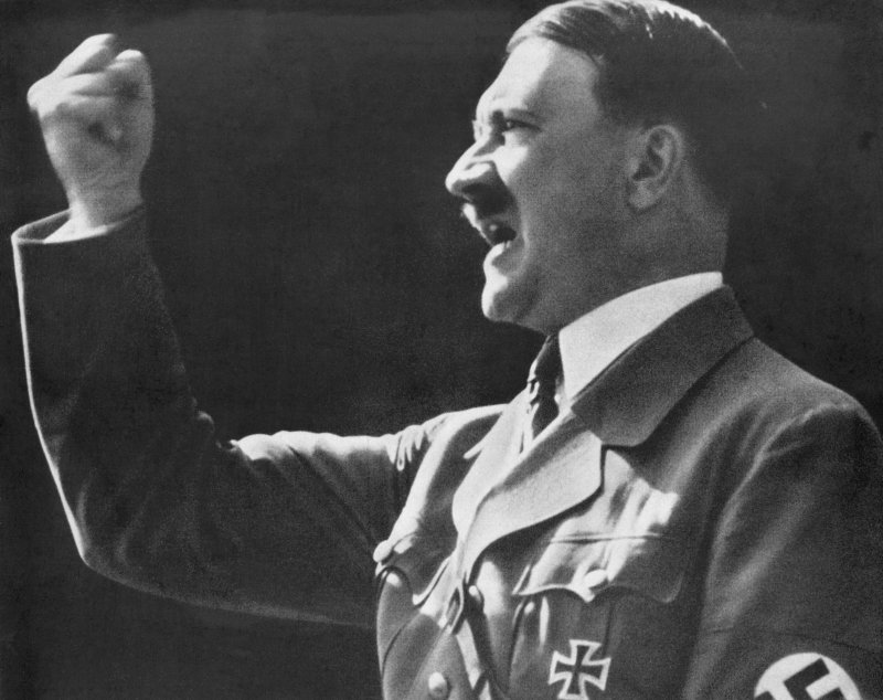 Adolf Hitler levanta um punho desafiador e cerrado durante um discurso. 