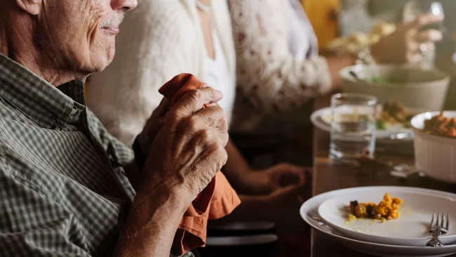 homem segurando guardanapo para limpar a boca após comer, sentado em uma mesa com prato com restos de comida e um garfo
