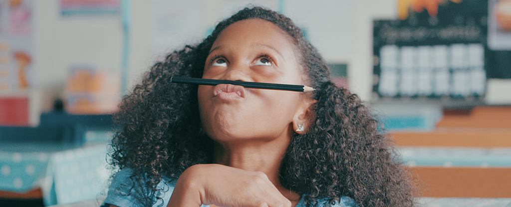 menina distraída segurando um lápis entre o lábio superior e o nariz olhando para cima
