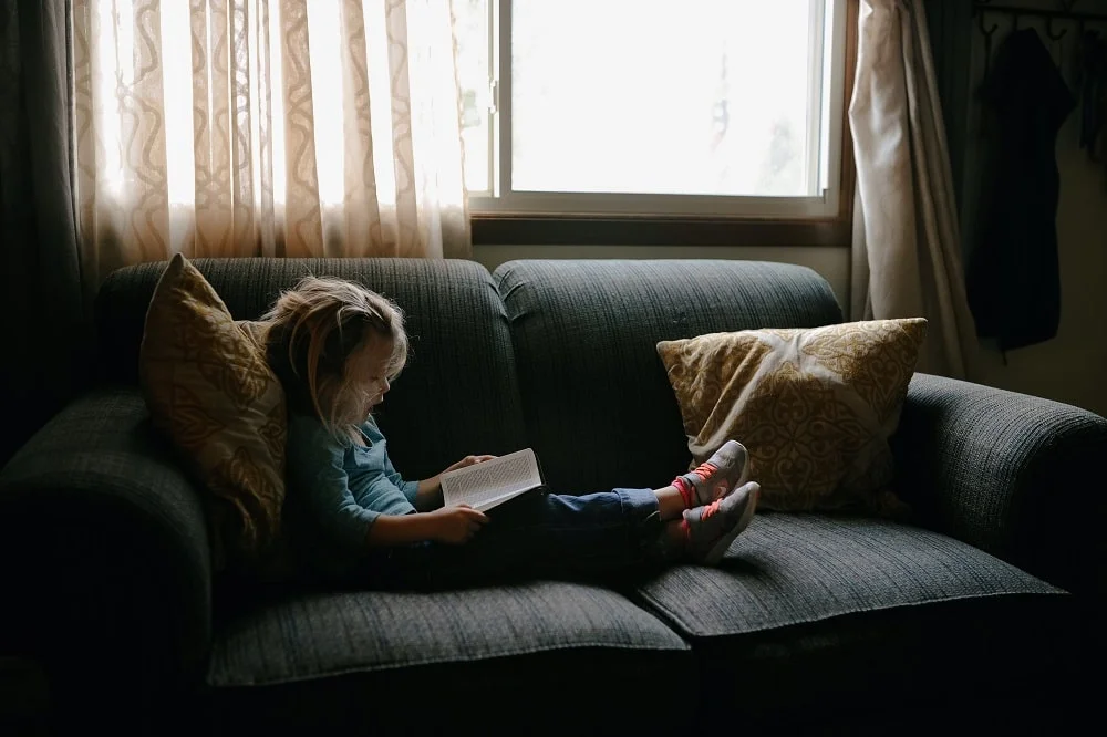 criança deitada em um sofá lendo um livro