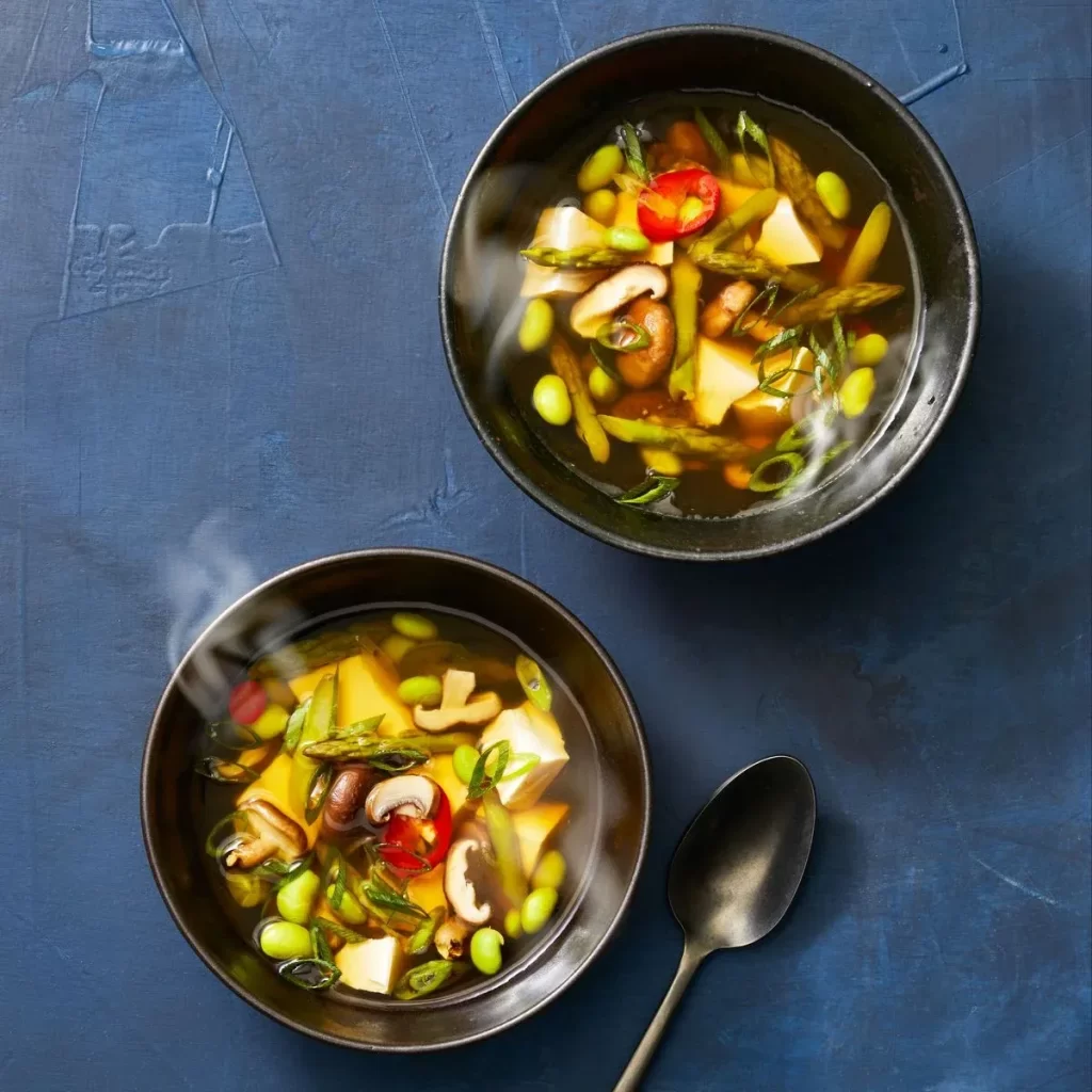 Dois pratos de sopa com legumes, cogumelos e grãos e uma colher