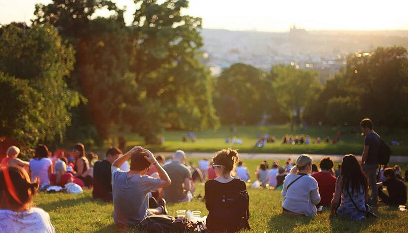 Pessoas sentadas em um gramado de um parque em um dia ensolarado