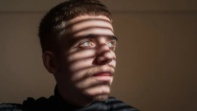 homem branco jovem olhando para luz com sombras ao fundo