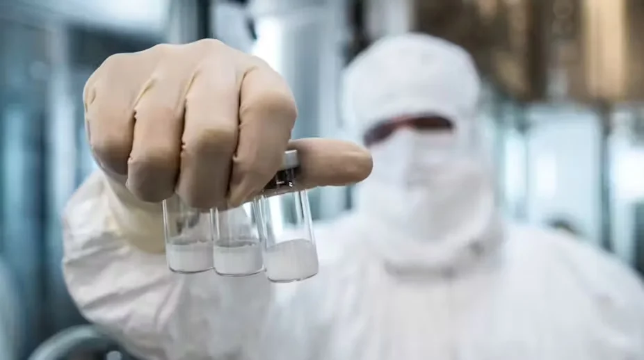 Técnico de laboratório com macacã o branco e máscara e luva segurando três frascos de vacina para dengue