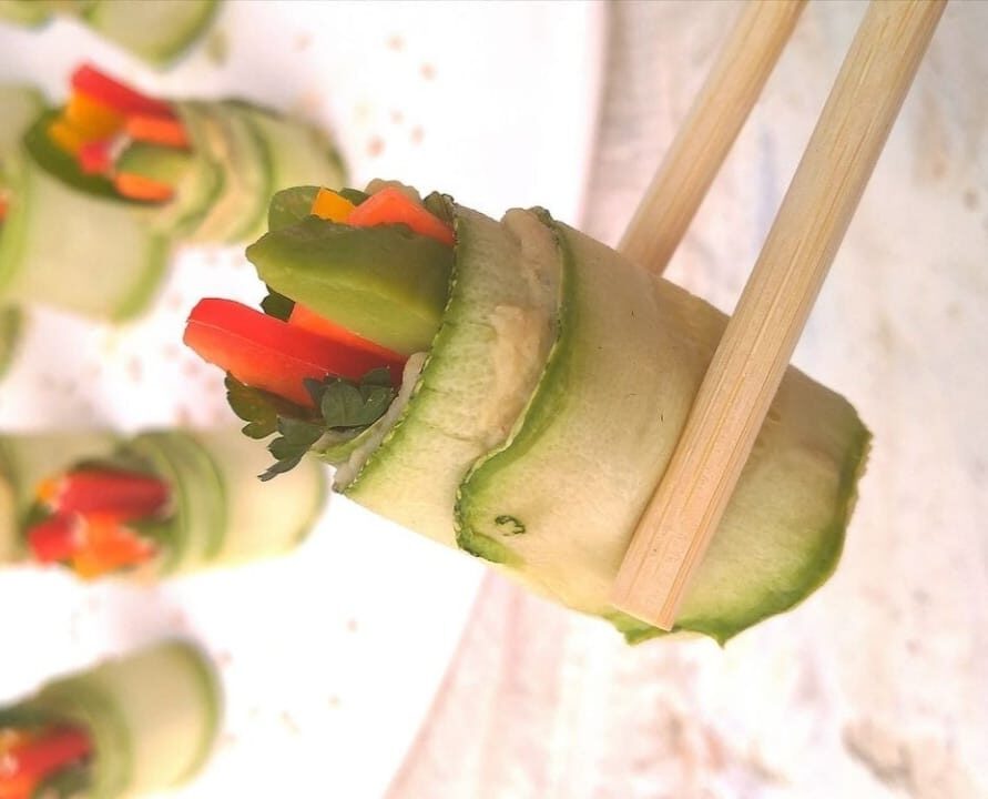 Hashis, palitos de sushi, segurando um rolinho de abobrinha recheado com vegetais